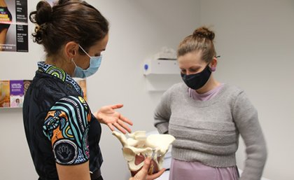 Two people wearing face masks looking at an anatomical model