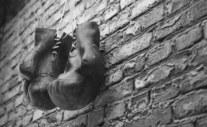 A black and white image of a pair of old leather boxing gloves hanging against a brick wall