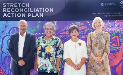 A man and three women stand on a stage in front of a UQ banner that reads Stretch Reconciliation Action Plan. 