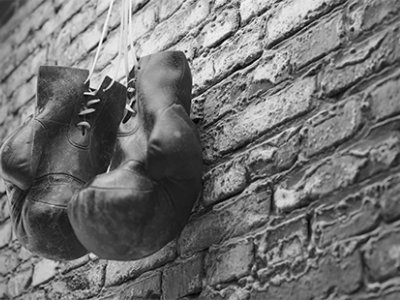 A black and white image of a pair of old leather boxing gloves hanging against a brick wall