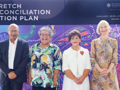 A man and three women stand on a stage in front of a UQ banner that reads Stretch Reconciliation Action Plan. 