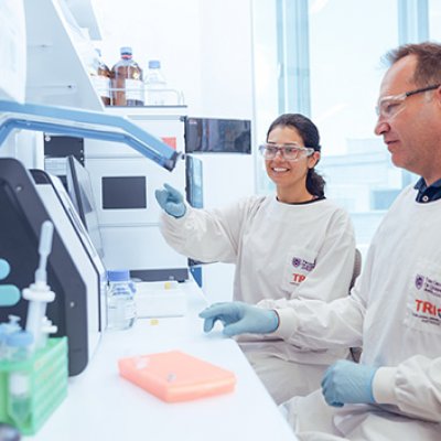 Two people in a science laboratory wearing lab coats while operating equipment