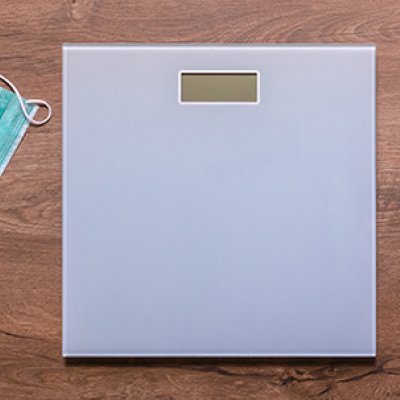 A weighing scale on a wooden floor next to a tape measure and a surgical face mask