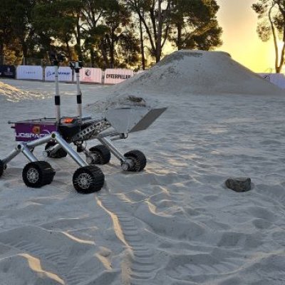 A four wheeled rover with an excavator attachment on a sandy field