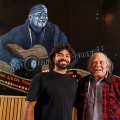 Thomas Scanlan, a young Indigenous man, with Kev Carmody, an older Indigenous man. They are standing in front of a large mural of Kev playing guitar.