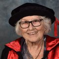 An older woman wearing a graduation gown and cap while smiling broadly