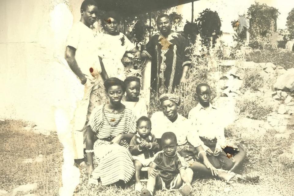 An old photo in sepia tones showing three generations of an African family outdoors.