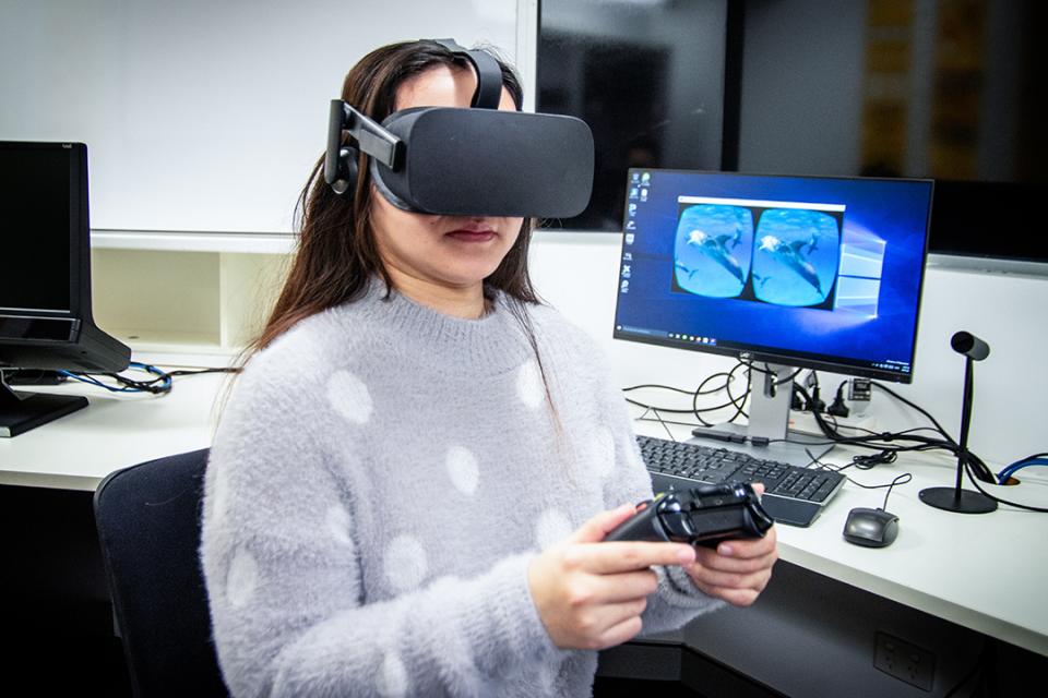 a woman in a grey sweater wearing VR goggles. 