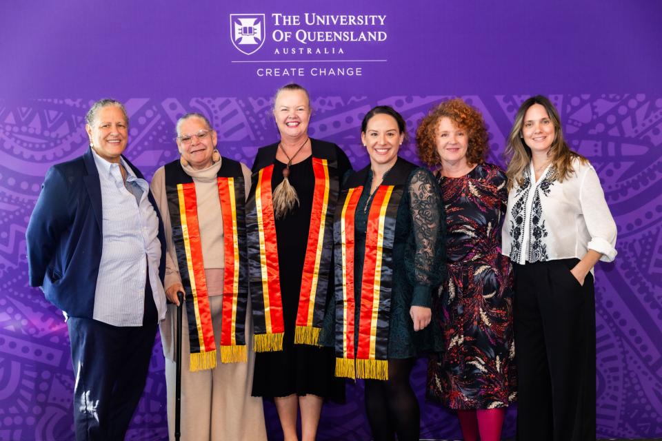 A group of women smiling at the camera in front of a purple backdrop.