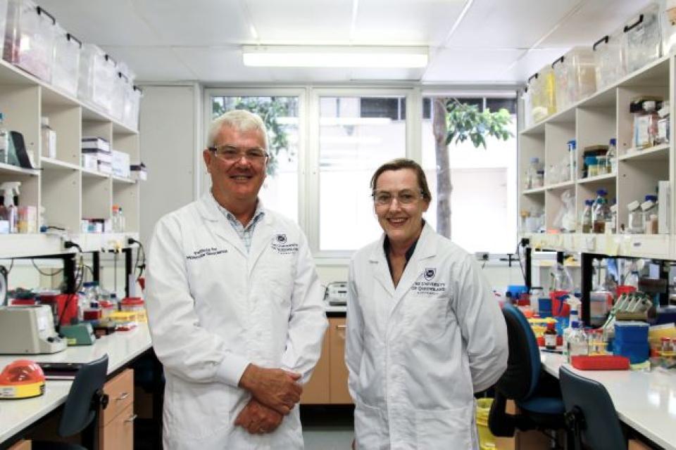 A man and woman in white lab coats stand in a lab smiling at the camera.