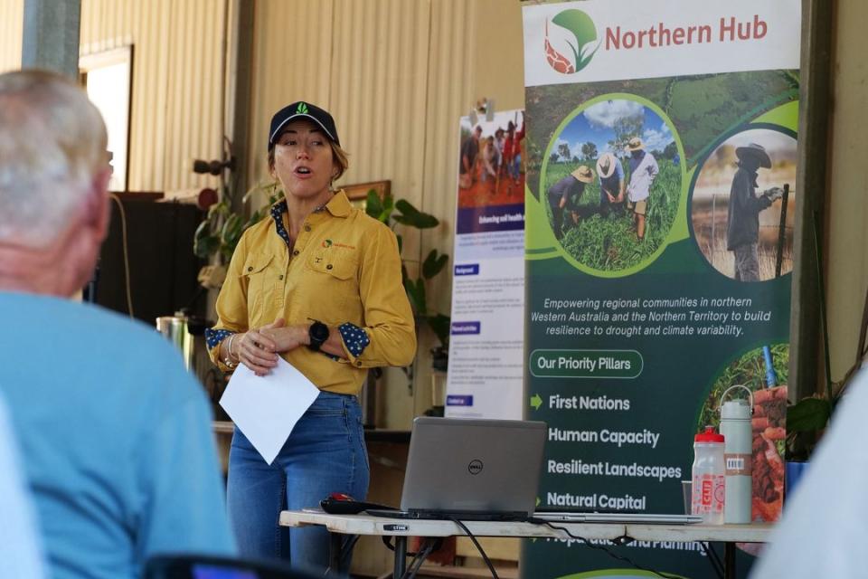 A woman weaing a baseball cap and wearing a yellow short speaks in front of a crowd