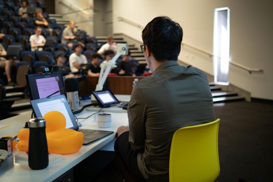 A lecturer addressing his students at the front of the room