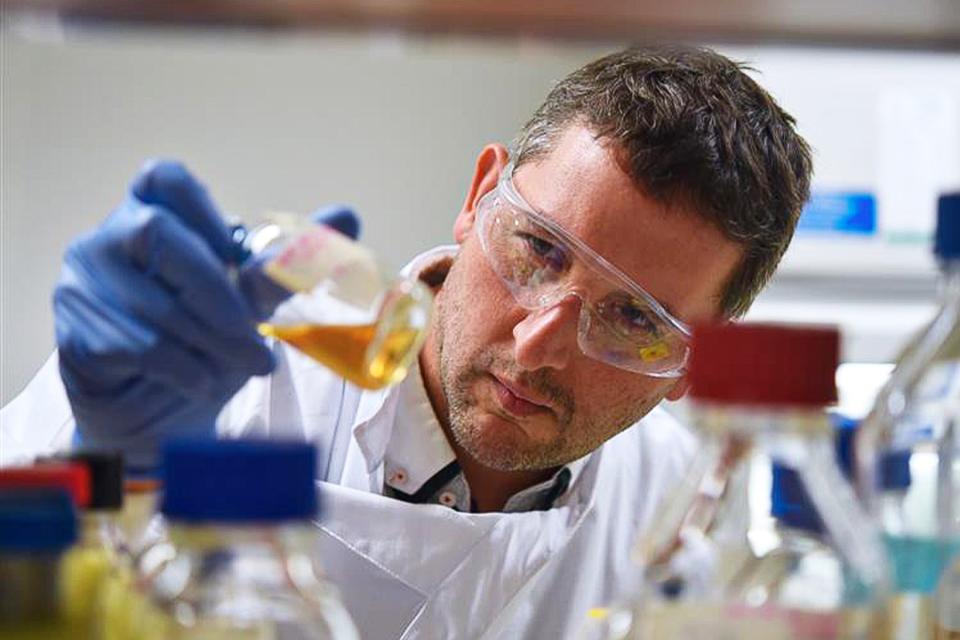 Professor Esteban Marcellin looking through a beaker in a lab.