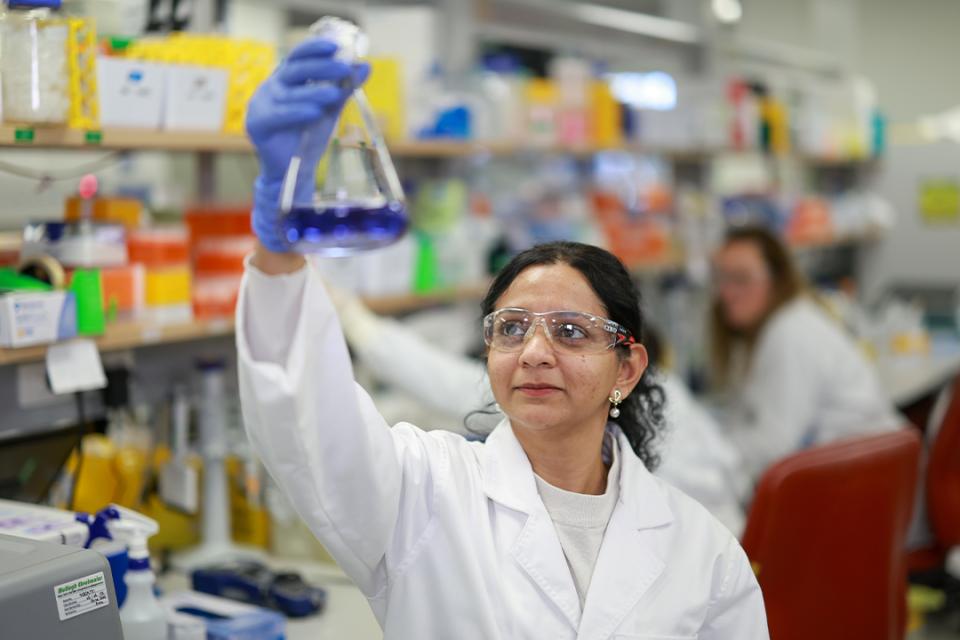 An image of a female scientist holding a beaker in a lab.
