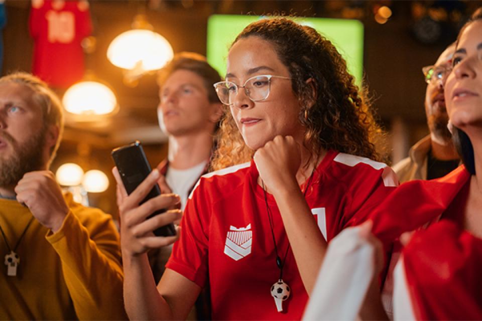 A female sports fan is in a crowd but cheering as she watches her phone