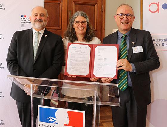 Three people standing behind a lecturn, one holding a document with a group of signatures