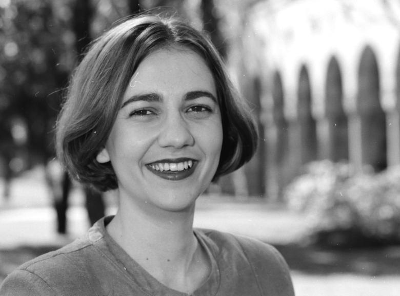 A black and white image of a woman with short hair standing in front of a sandstone building