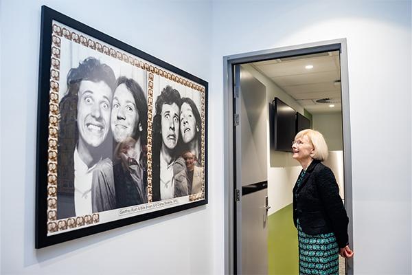 Professor Deborah Terry AC looking at images of Geoffrey Rush and Bille Brown on the wall.
