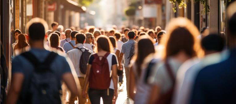 In a busy street, lit by late afternoon sun, all kinds of people go about their business.