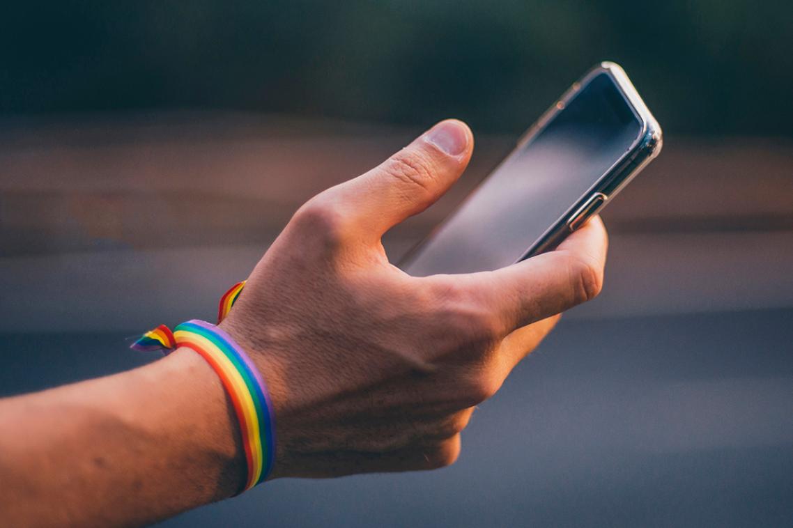 A hand with a rainbow bracelet holds a mobile phone.