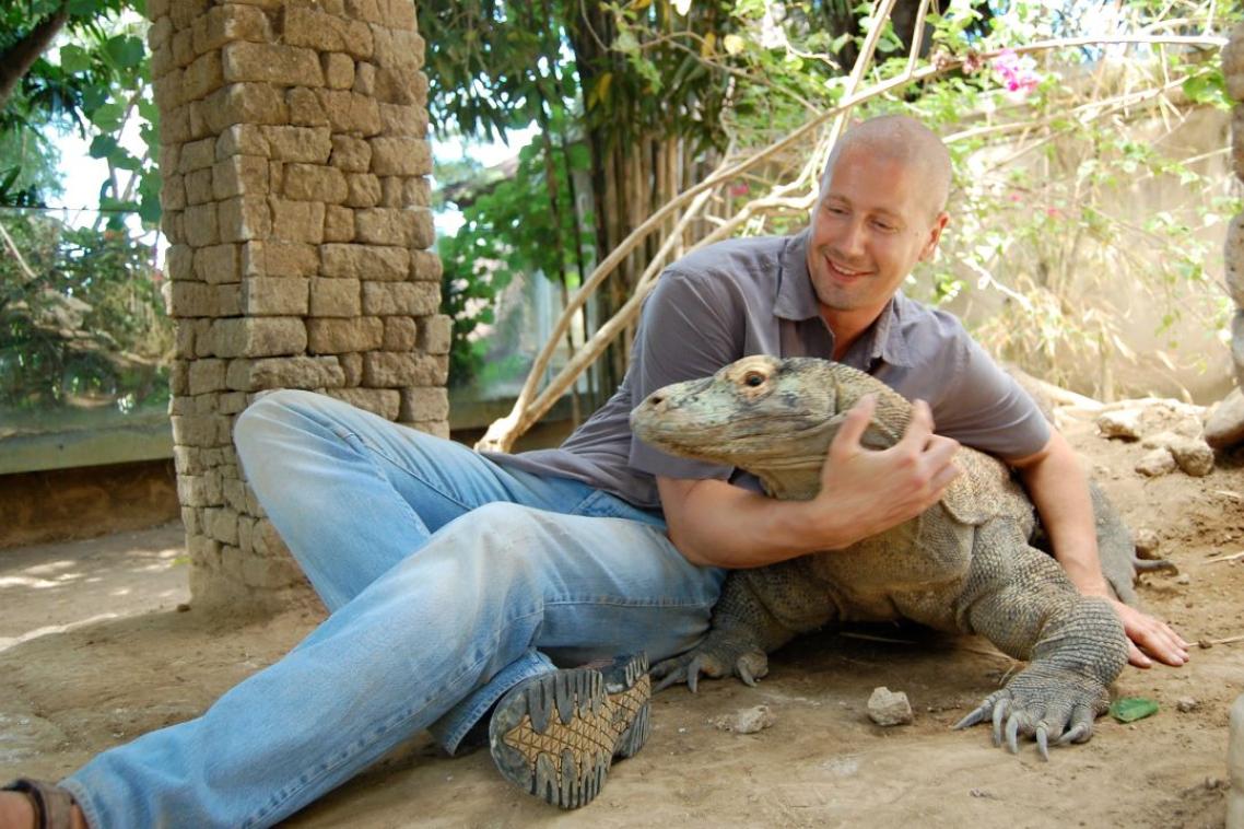 A man lying on the ground holding a komodo dragon