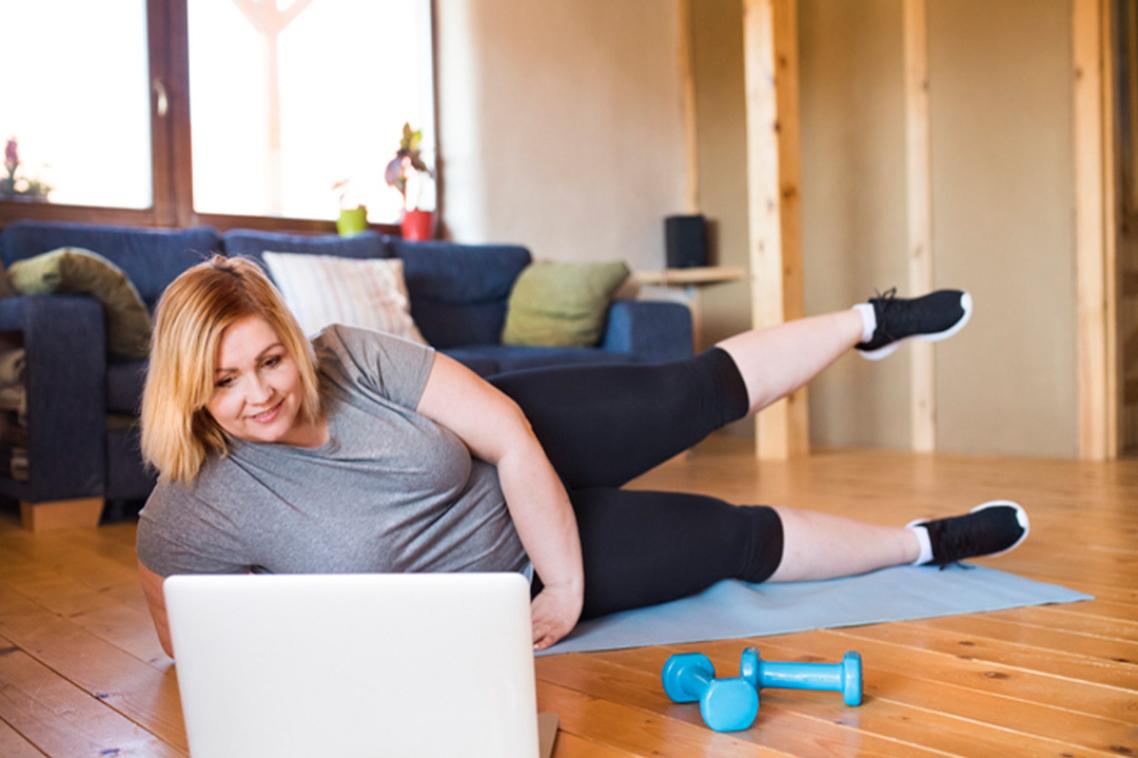 An obese woman does floor exercises in a loungeroom.