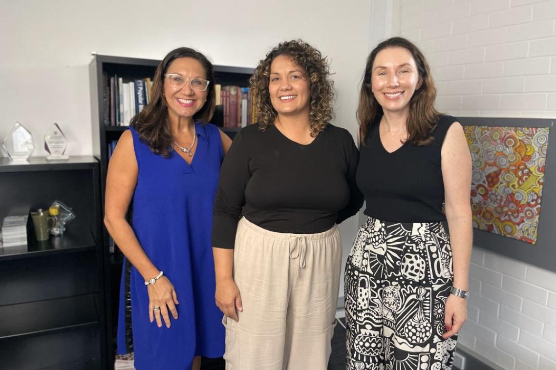 Three women standing in a row smiling at the camera in a film studio