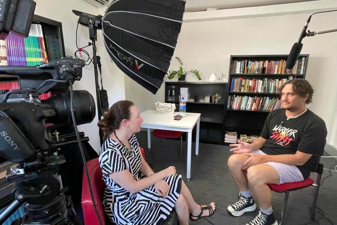 Two people sitting across from eachother surrounded by lights and a camera