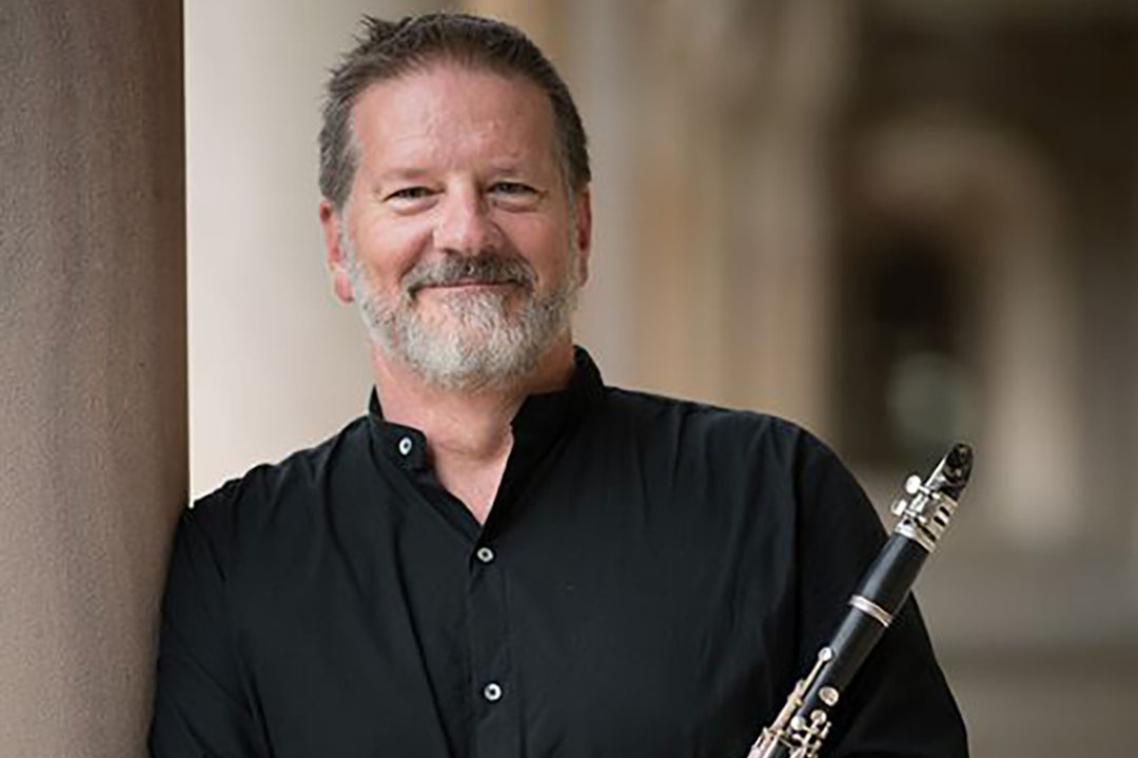 A man leaning on a sandstone pillar holding a clarinet.