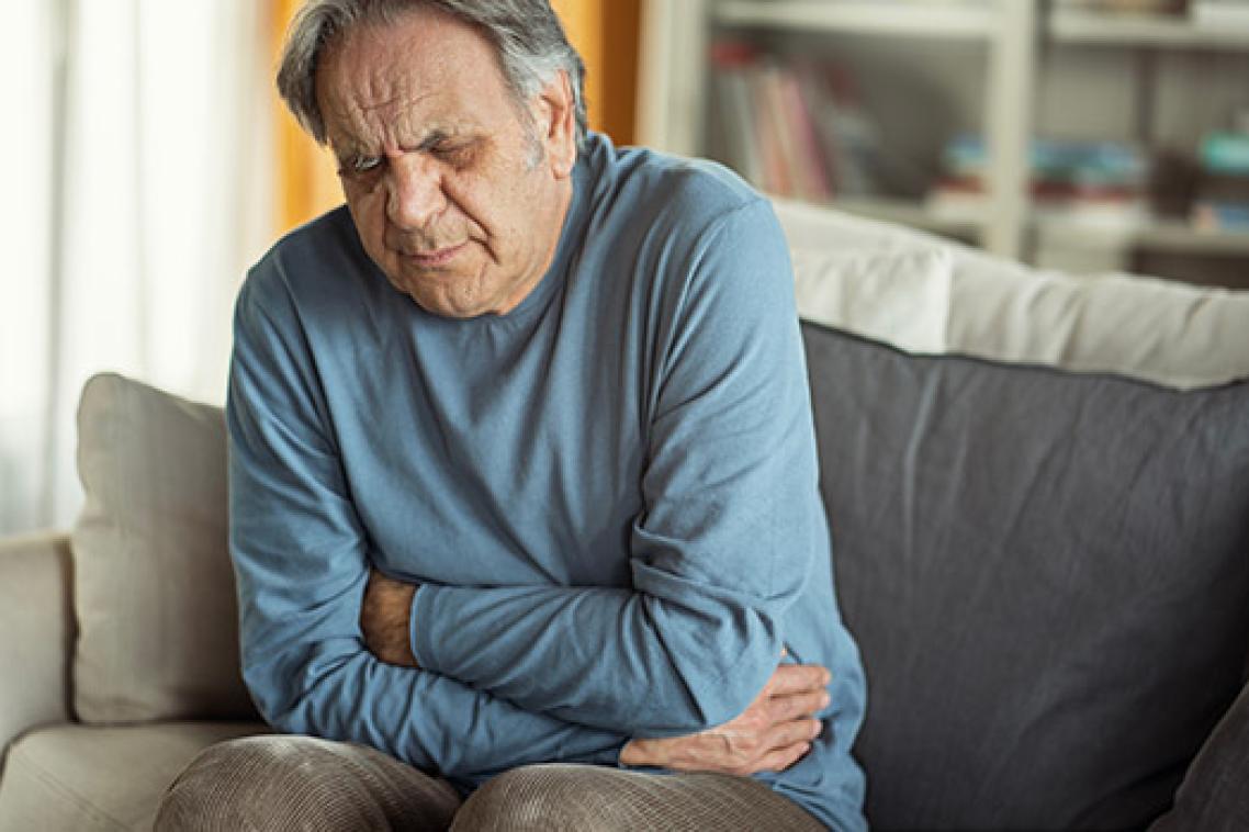 man holding lower abdomen, grimacing in pain