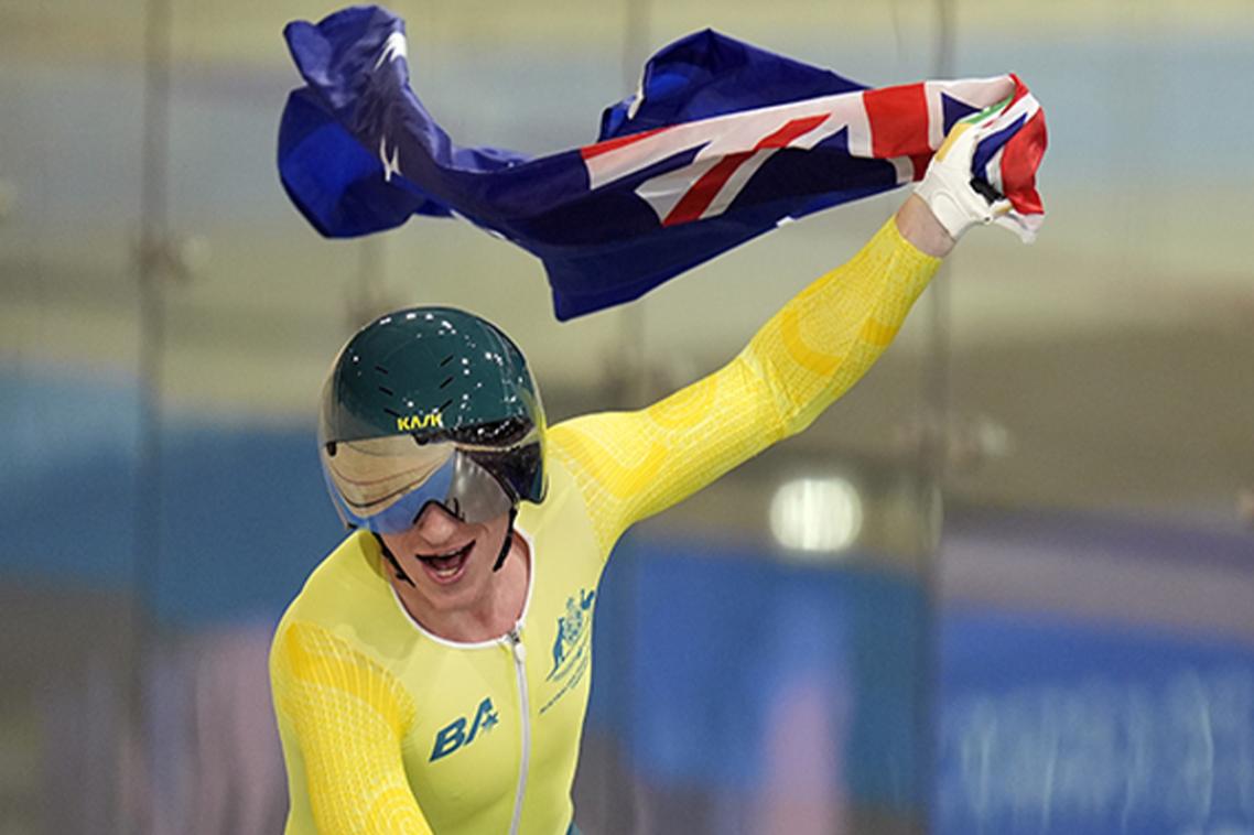 A male cyclist in green and gold holds up the Australian flag.