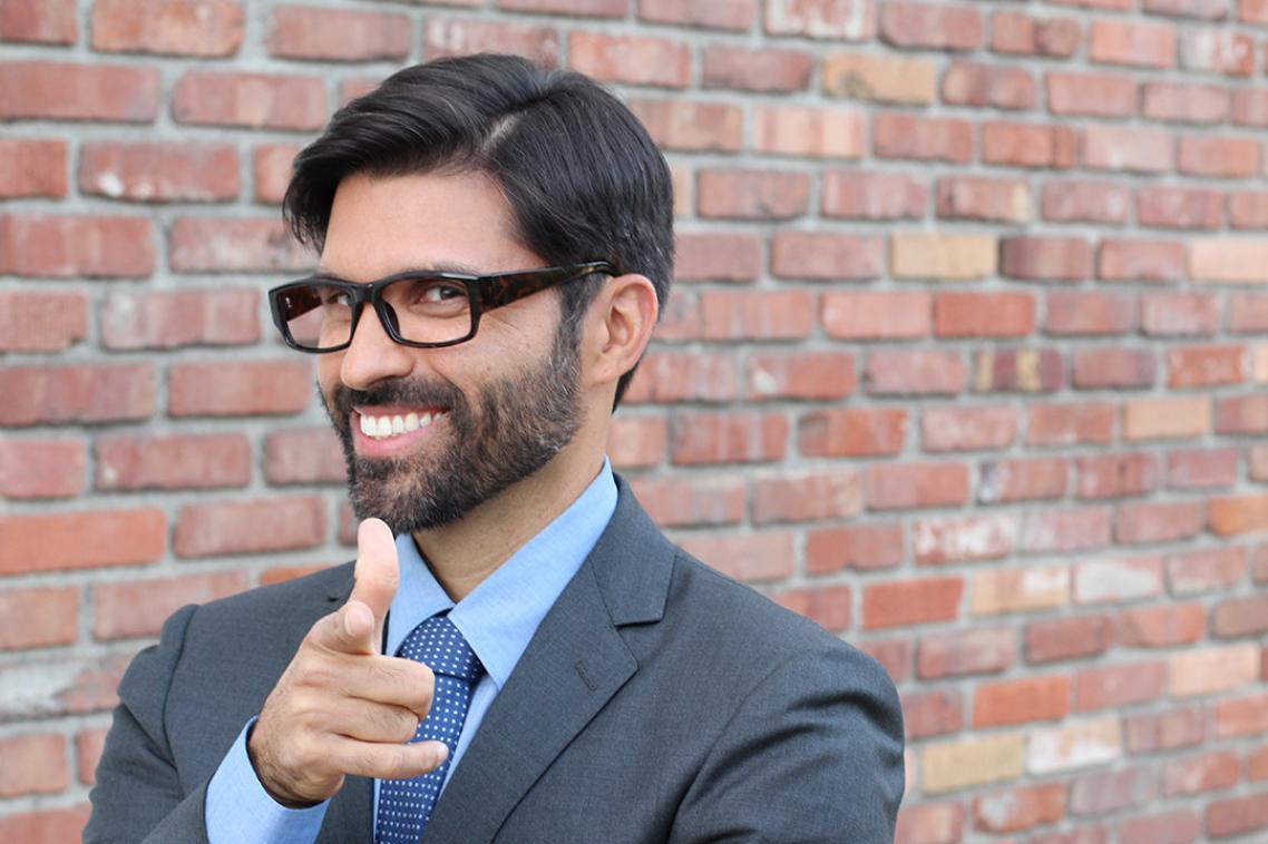 An arrogant man in a suit and glasses smiles at the camera.