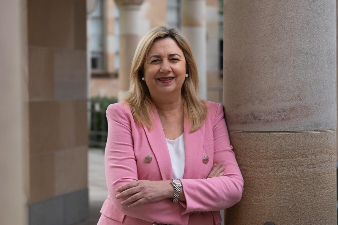 A woman in a pink blazer leaning against a sandstone pole