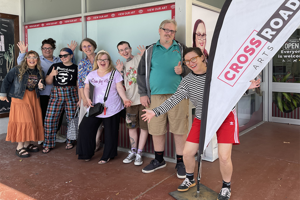A group of people smiling at the camera holding a flag that says "Cross Roads".