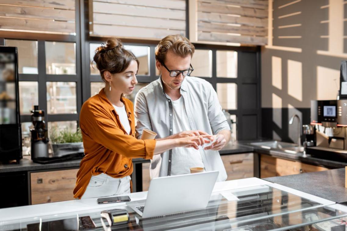 A man and a woman stand in an office next to a laptop
