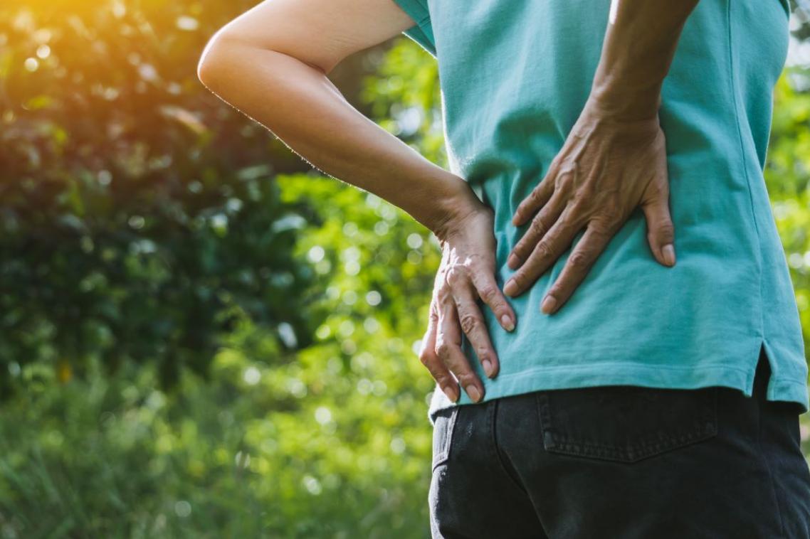 Woman in a blue t-shirt holding her lower back.