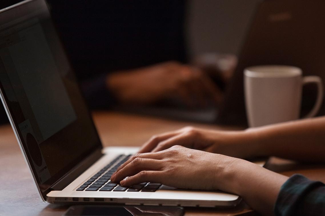 A laptop on a desktop with hands typing.