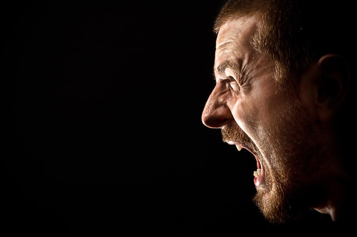 A profile photo of a man yelling with his mouth open against a black background.