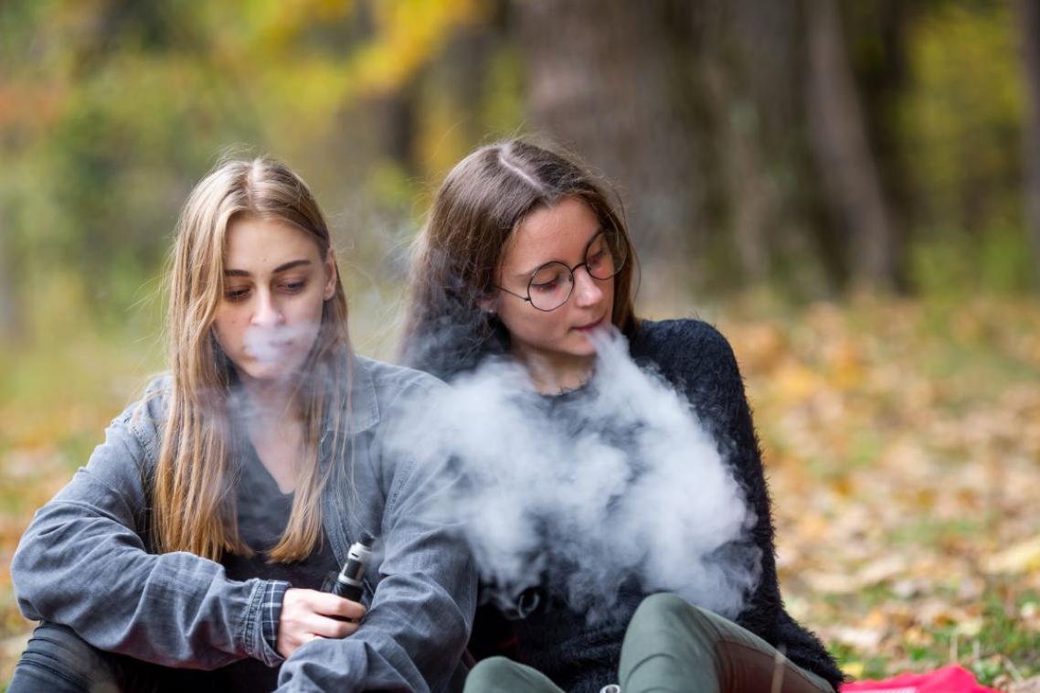 Two young women using vapes outdoors.