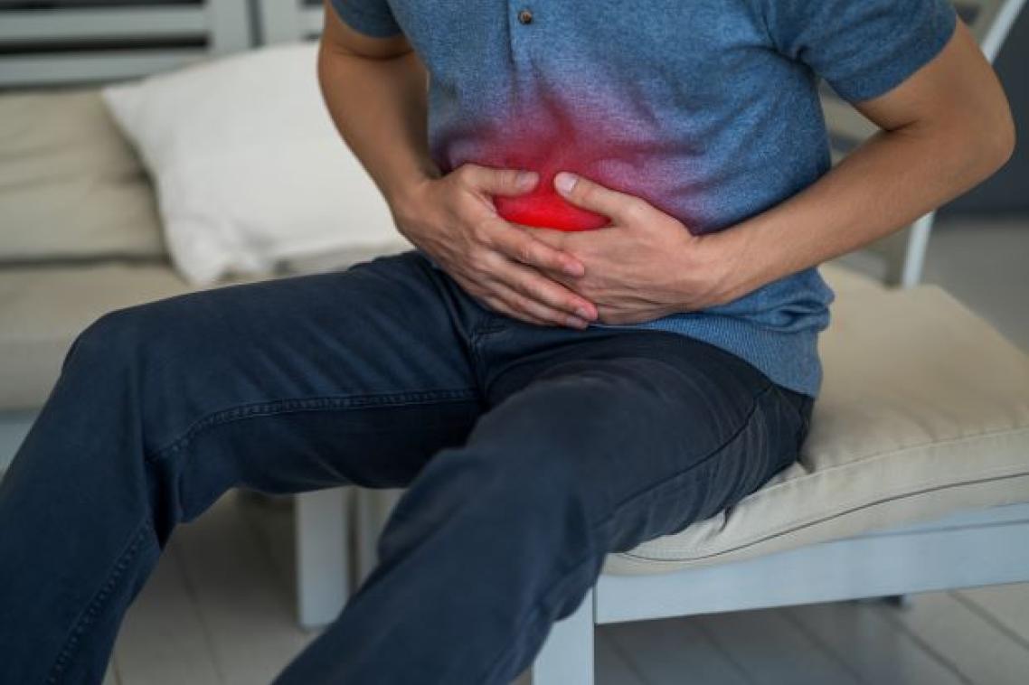 A person in a blue shirt clutches their abdomen which is highlighted with a red light