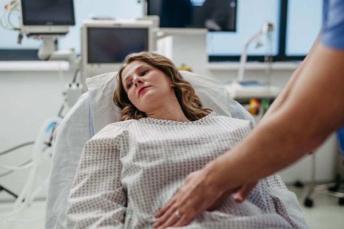Woman lying in hospital bed being examined by doctor. Adobe.