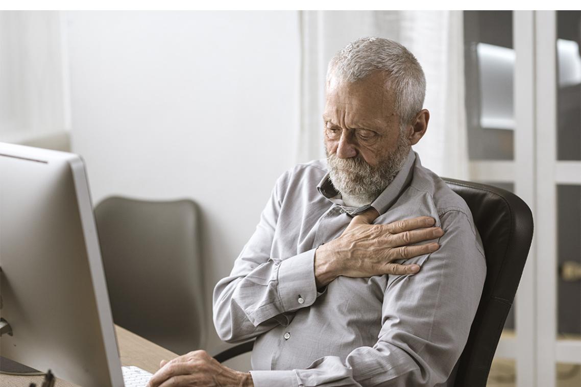 An older man sitting down clutching at his heart.