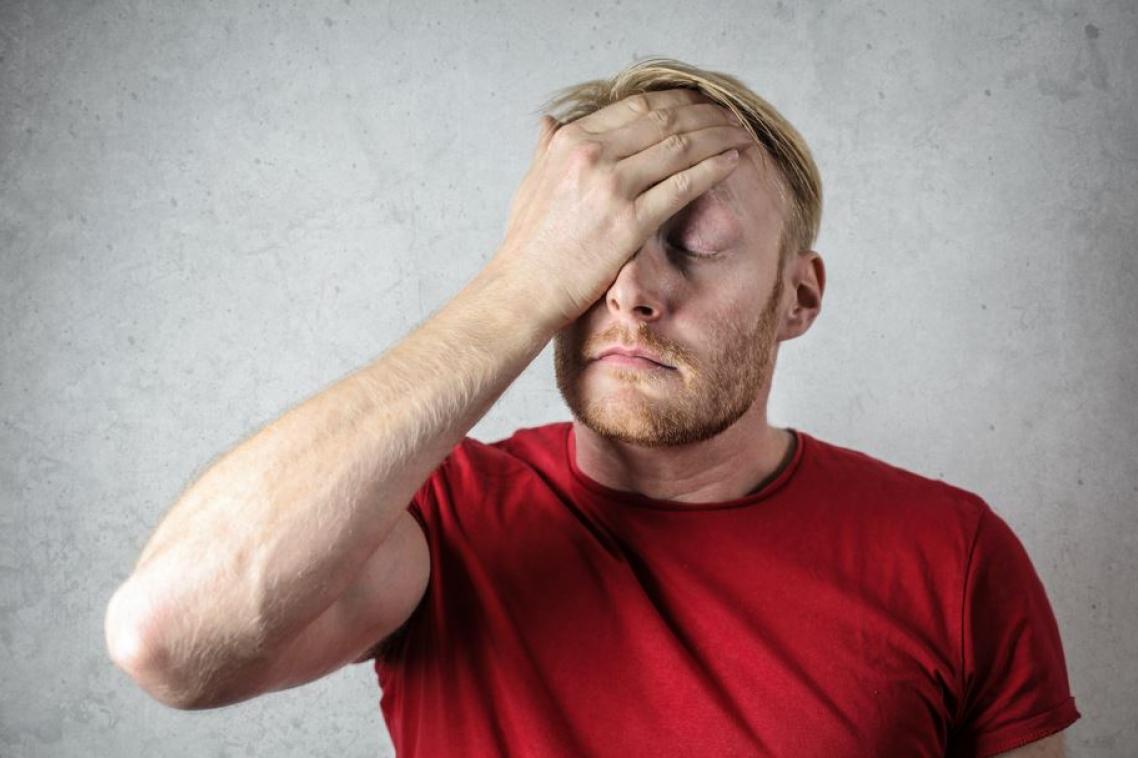A man in a red shirt holding his head in pain.