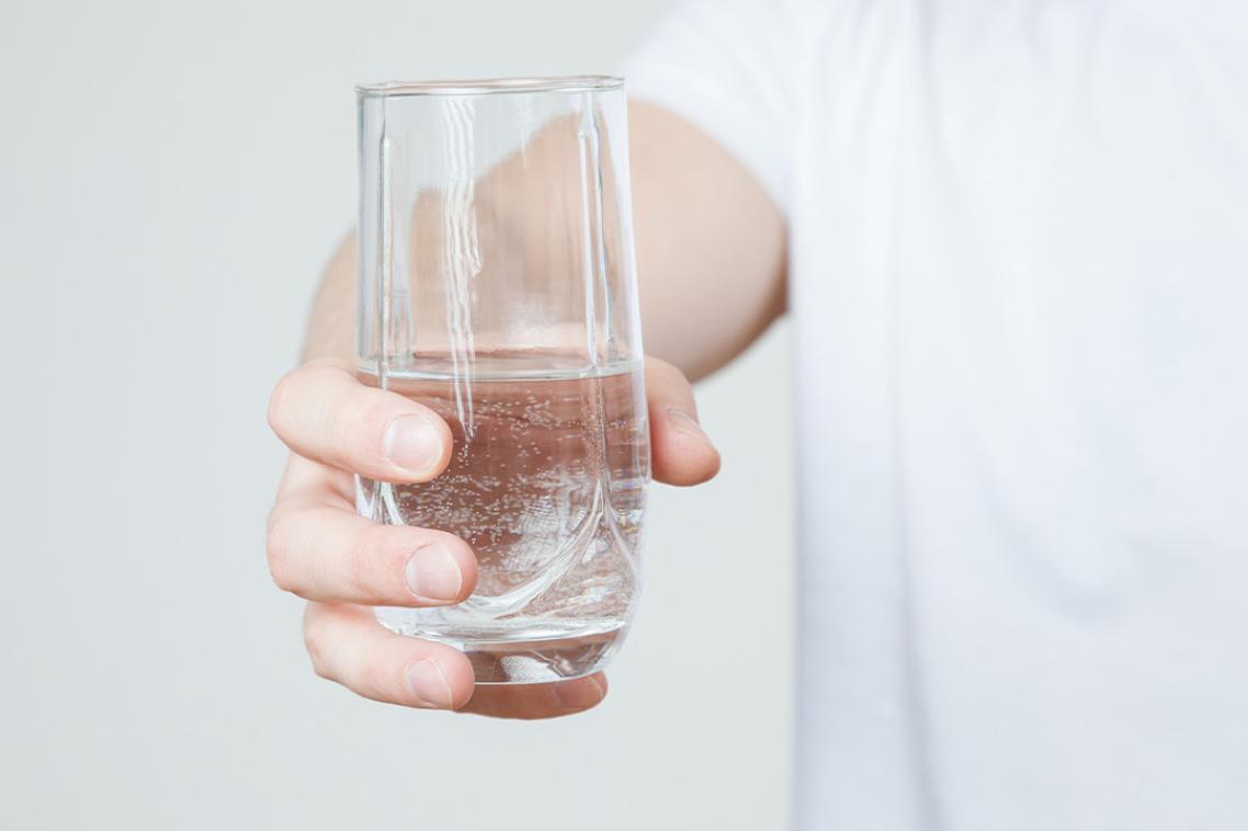 A hand holds a glass of bubbly water.