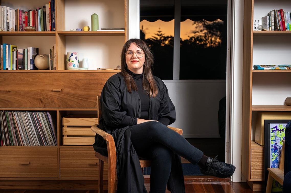 A woman sitting in front of a bookcase and a artwork on the wall 