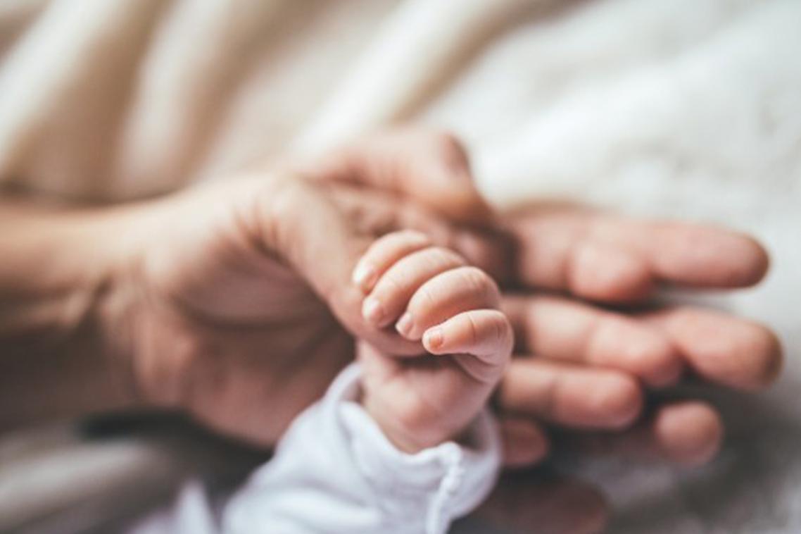A baby's hand holds onto the thumb of an adult hand.