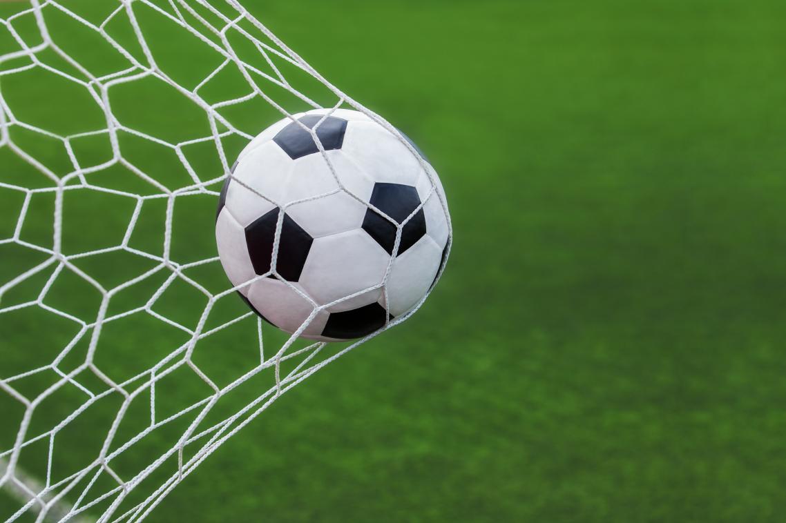 A black and white soccer ball going into the back of a white net.