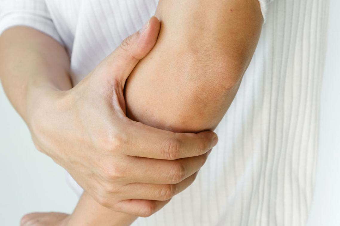 A man in a white shirt holding his elbow.