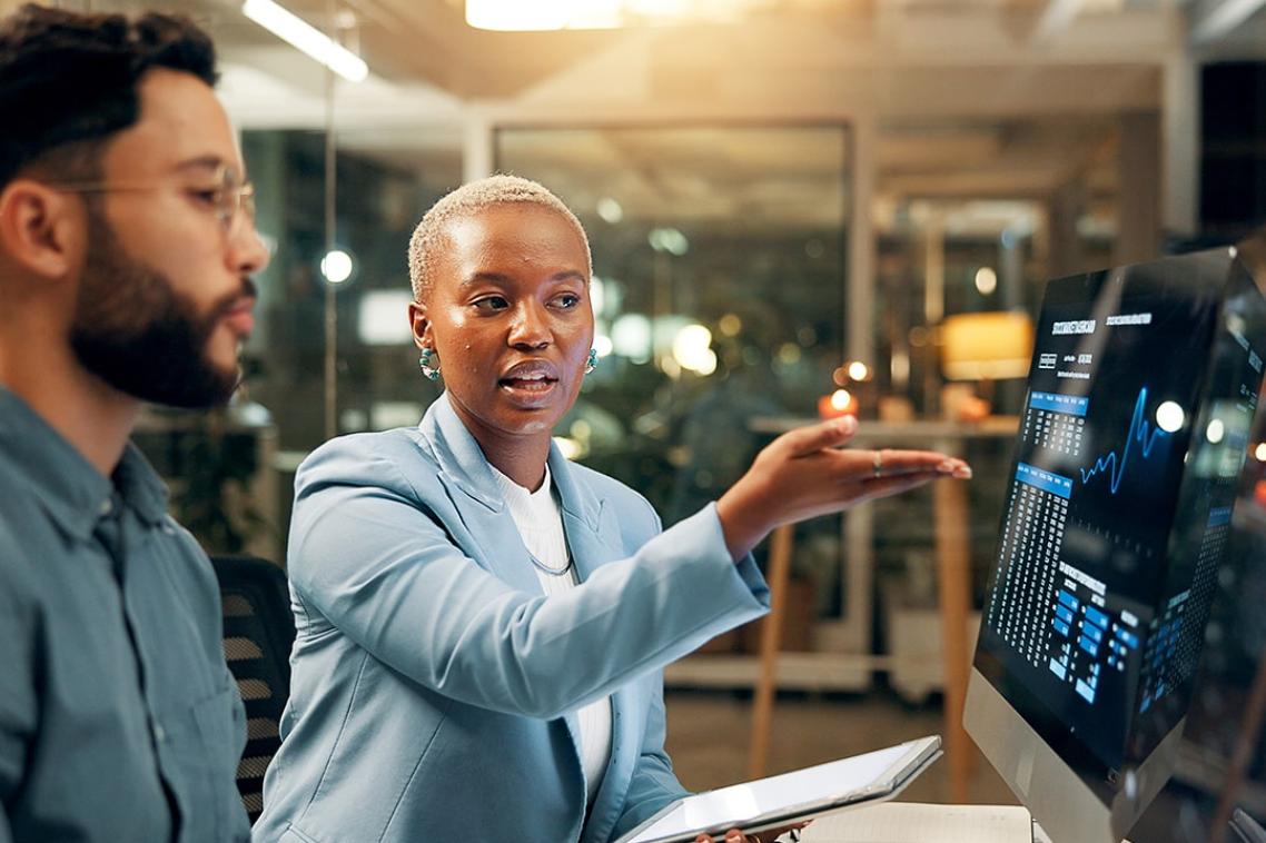 A woman explains information on a computer screen to her colleague.