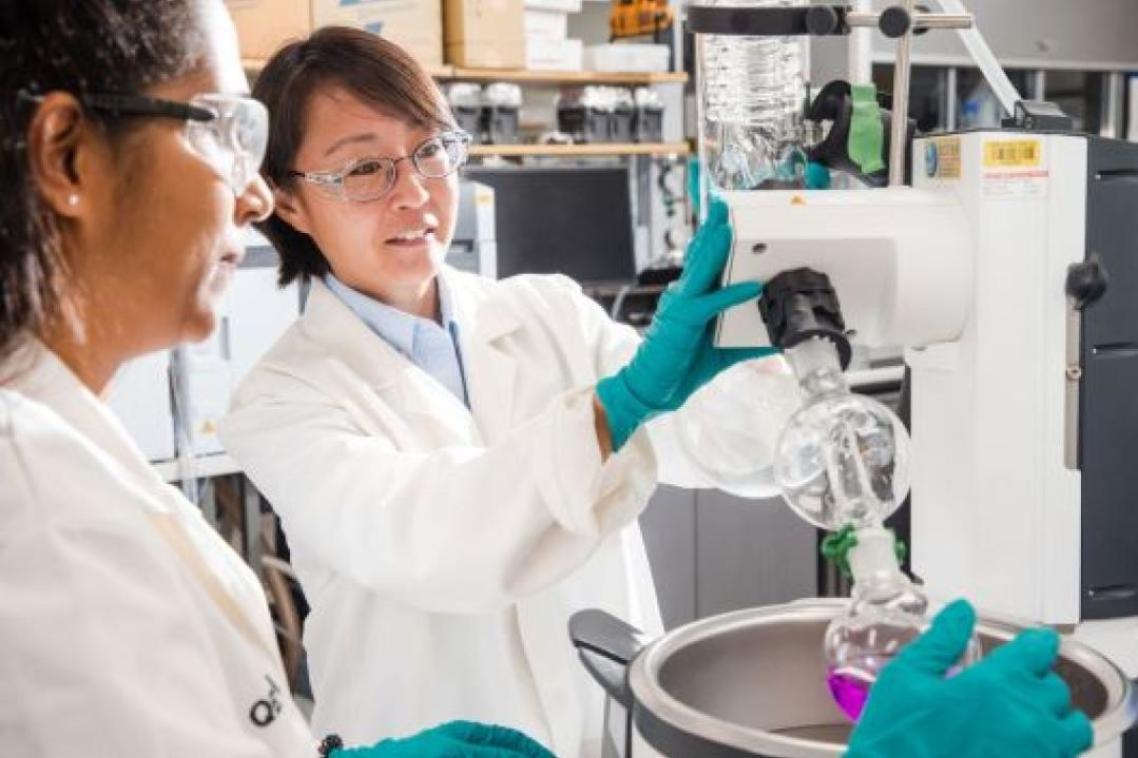2 female scientists in white lab coats study an experiment in a laboratory.